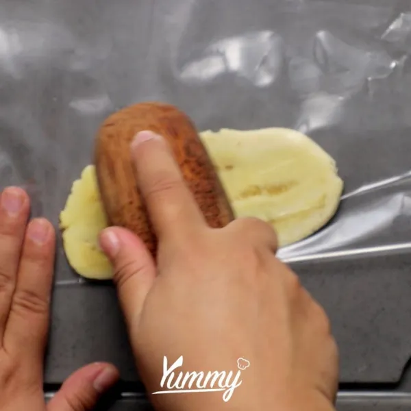 Belah pisang menjadi dua bagian, masukkan di plastik, pipihkan menggunakan uleg.