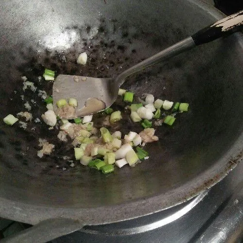 Tumis bawang putih yang sudah halus sambil gunting tipis bawang prei ke dalam wajan.