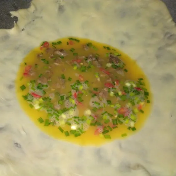 Letakkan adonan yang sudah tipis di atas wajan. Masukkan telur, lalu lipat membentuk persegi.