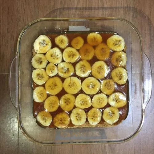 Tuang lapisan karamel ke dalam pireks yang telah berisi lapisan biskuit dan pisang, tuang menggunakan sendok dan ratakan.
