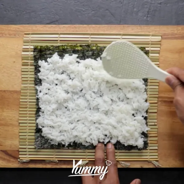 Siapkan satu lembar nori, letakkan nasi di atasnya. Tekan-tekan nasi hingga benar-benar tipis.