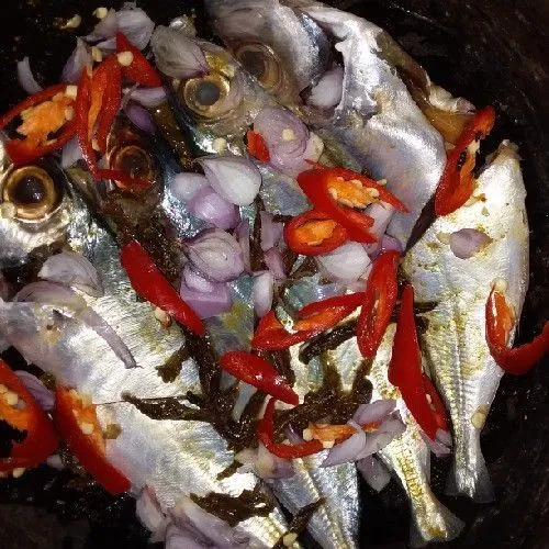 Masukkan ikan ke dalam kuali berisi campuran pacukka, kunyit, dan garam. Tambahkan irisan bawang merah dan cabe.