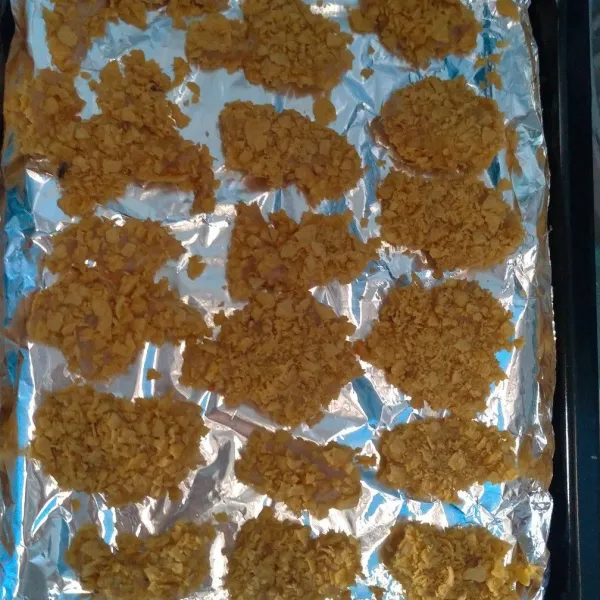 Masukkan ayam ke telur kemudian balurkan di corn flakes. Tata di atas loyang.