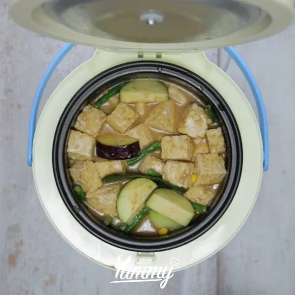 Buka tutup rice cooker, masukkan labu siam, kacang panjang, jagung, melinjo, tempe, terong, gula, dan garam. Masak selama 5 menit.