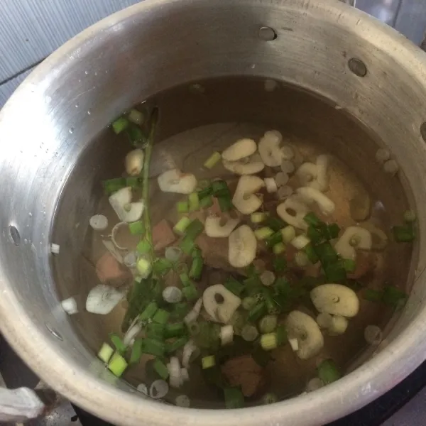 Masukkan daging ke dalam panci yang sudah di isi air. Rajang bumbu seperti: bawang putih dan daun bawang.
