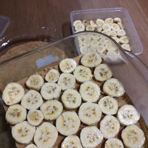 Untuk lapisan kedua, potong-potong pisang sesuai selera, kemudian tata dipireks yang berisi adonan biskuit. Sisihkan.
