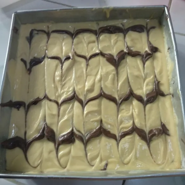 Siapkan loyang ukuran 24x24 lapisi dengan margarin dan tepung. Masukkan adonan putih dan coklat berselang seling secara acak ke dalam loyang. Buat motif marble / marmer dengan bantuan tusuk sate / pisau.