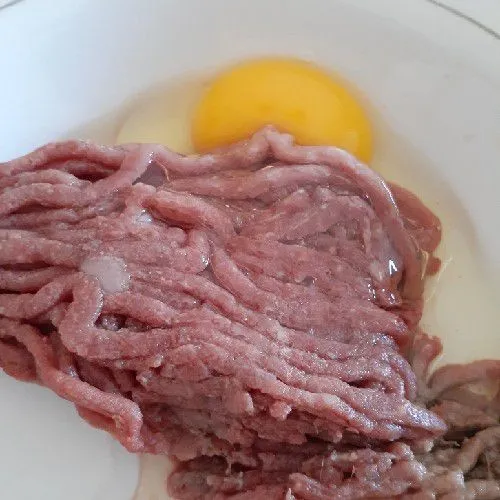Bahan bakso daging: Pecahkan telur dan taruh di piring berisi daging sapi giling.