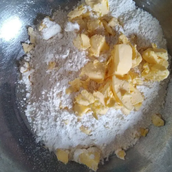 Campur tepung terigu, margarin beku dan gula halus, aduk rata hingga berbutir-butir. Tambahkan air, aduk rata lalu gilas.