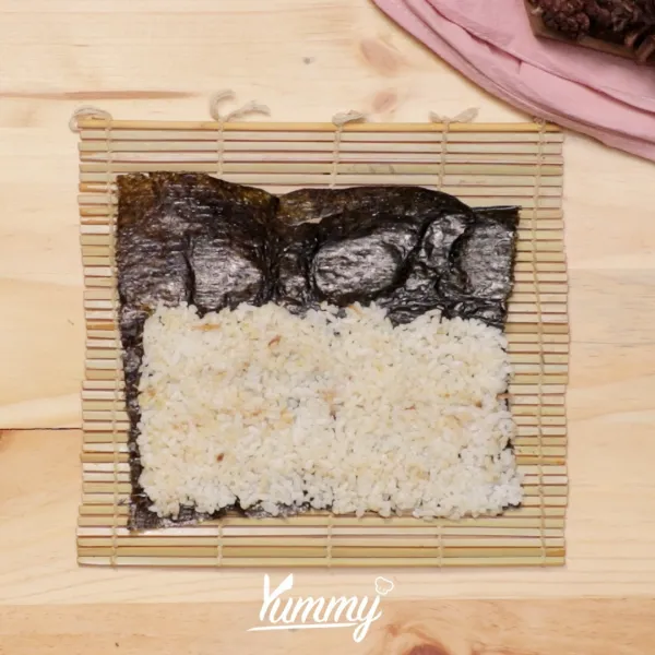 Siapkan 1 lembar nori lalu tambahkan nasi kuning di atasnya dan pipihkan (usahakan sangat pipih atau tipis hingga norinya terlihat).