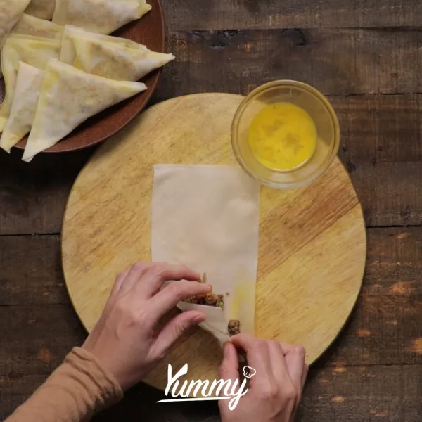 Letakkan bahan isian ke dalam kulit spring roll, bentuk menjadi segitiga dan rekatkan dengan telur.