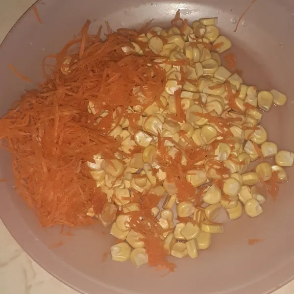 Pipil jagung, parut wortel kemudian cuci bersih dan tiriskan, masukkan ke dalam wadah.