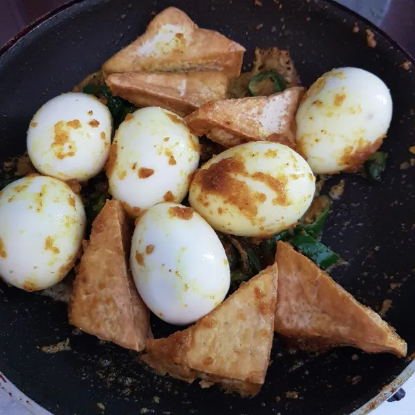 Setelah bumbu matang, masukkan telur rebus dan tahu goreng, aduk rata.