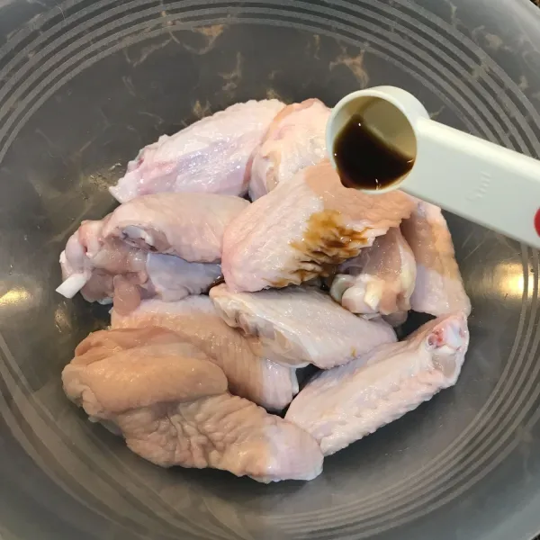 Masukkan potongan ayam di dalam wadah, beri kecap asin.