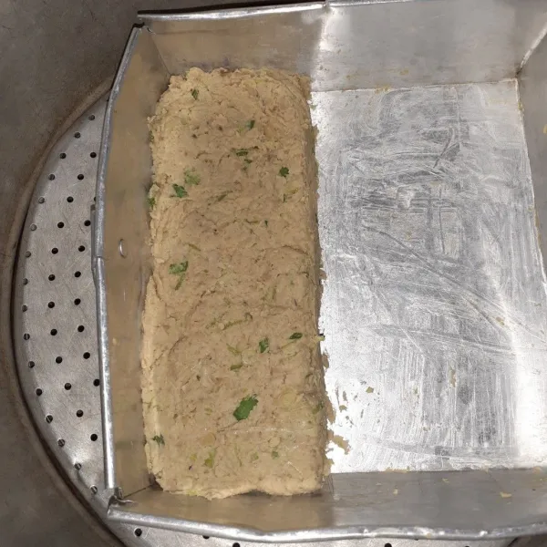 Panaskan panci, masukkan adonan tempe ke dalam loyang, ratakan, lalu kukus hingga tempe lembut dan berubah warna.