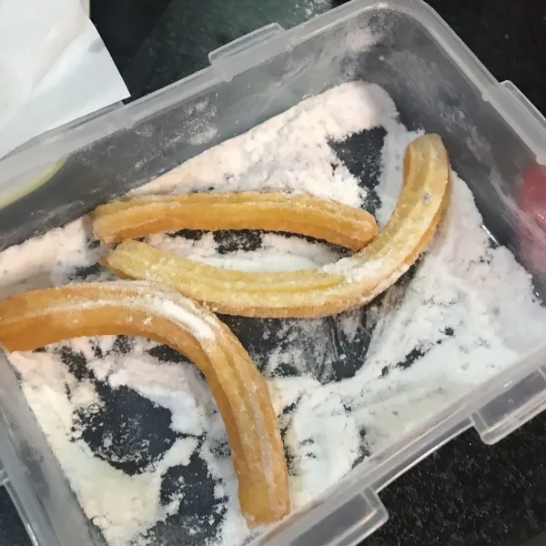 Setelah diangkat, gulingkan churros kedalam gula halus.