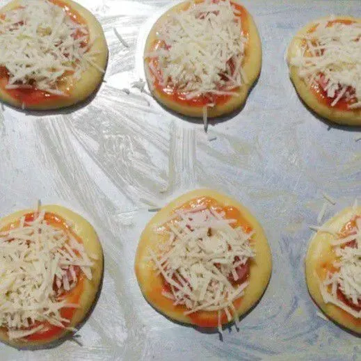 Oles adonan dengan saos sambal, beri irisan sosis dan terakhir taburi dengan keju cheddar parut. Panggang adonan selama 25 menit.