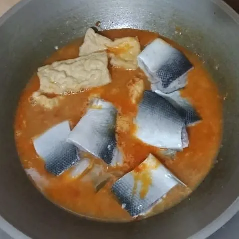 Masukkan air, masak hingga mendidih, lalu masukkan ikan bandeng dan tahu goreng. Aduk sebentar, lalu masukkan garam dan gula.