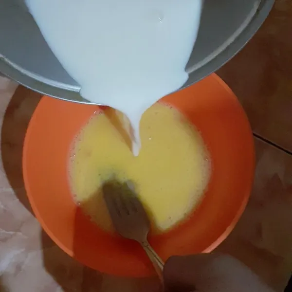 Tuang susu panas ke dalam kocokan telur sambil terus diaduk.