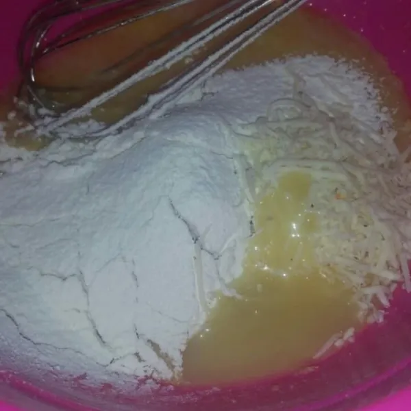 Ayak tepung terigu dan baking powder, masukkan dalam wadah bersama dengan keju parut dan susu kental manis. Aduk sampai tercampur rata.