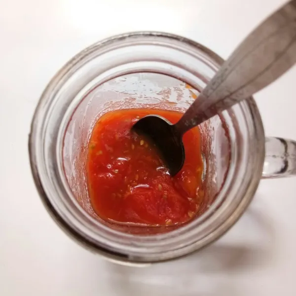 Masukkan tomat ke dalam gelas. Tambahkan gula pasir, lalu haluskan tomat dengan sendok hingga hancur.