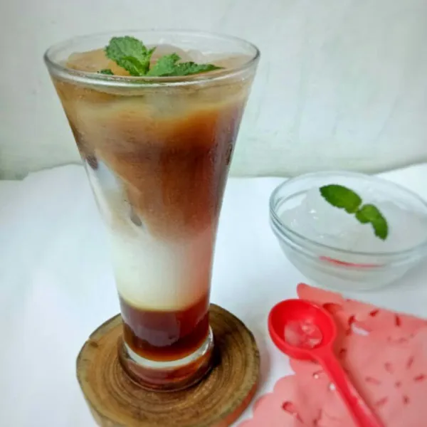 Tata di gelas dengan membuat layer cairan gula, susu cair, cairan kopi, dan terakhir tambahkan es batu. Sajikan.