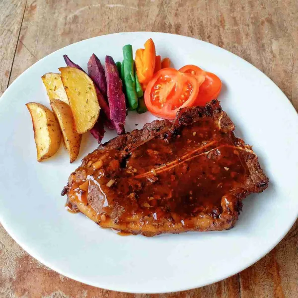 Sajikan T-bone Steak, siram dengan saus lada hitam dan beri pelengkapnya seperti karbo dan sayuran.