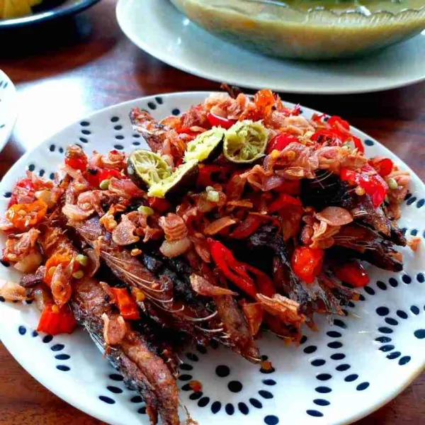 Tata tongkol goreng di piring saji lalu taburi dengan sambal mbe dan perasi dengan jeruk limau. Sajikan.