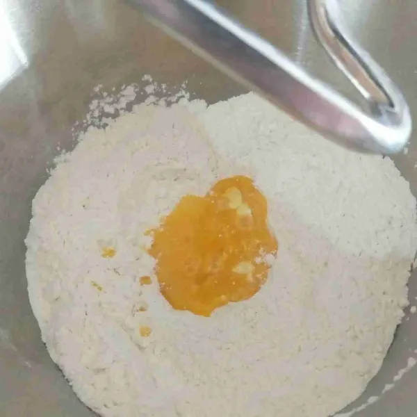 Pada mangkuk, campur tepung terigu, sisa gula pasir, dan garam. Beri kocokan telur ditengahnya.