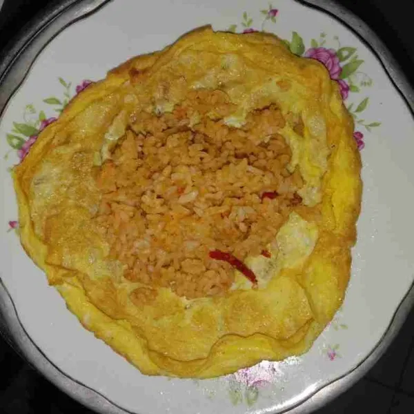 Letakkan omelette di atas piring saji, tambahkan nasi goreng dibagian tengah omelette kemudian lipat kanan kiri hingga rapi.