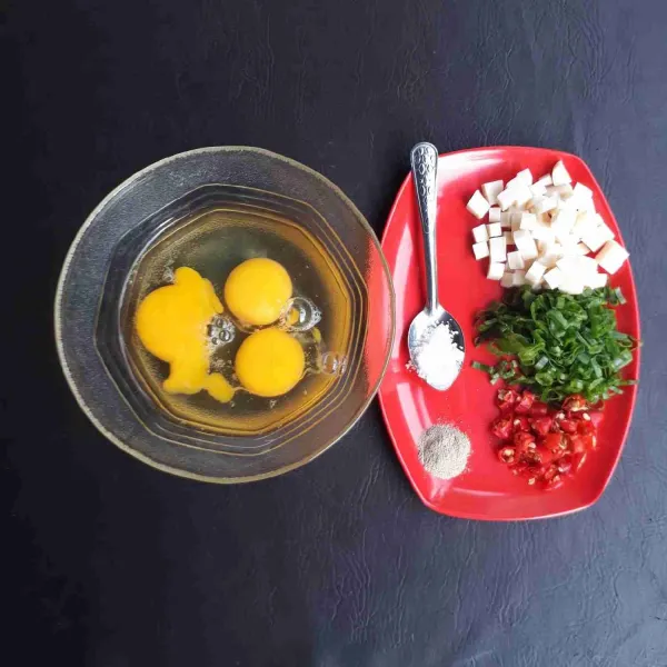 Siapkan bahan-bahan yang akan dimasak, masukkan telur dalam mangkuk. Potong dadu kecil keju dan iris tipis daun bawang serta cabe rawit.