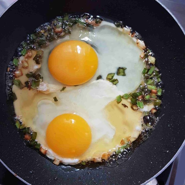 Goreng dua butir telur diatas irisan daun bawang lalu siram-siram dengan minyak hingga telur setengah matang.