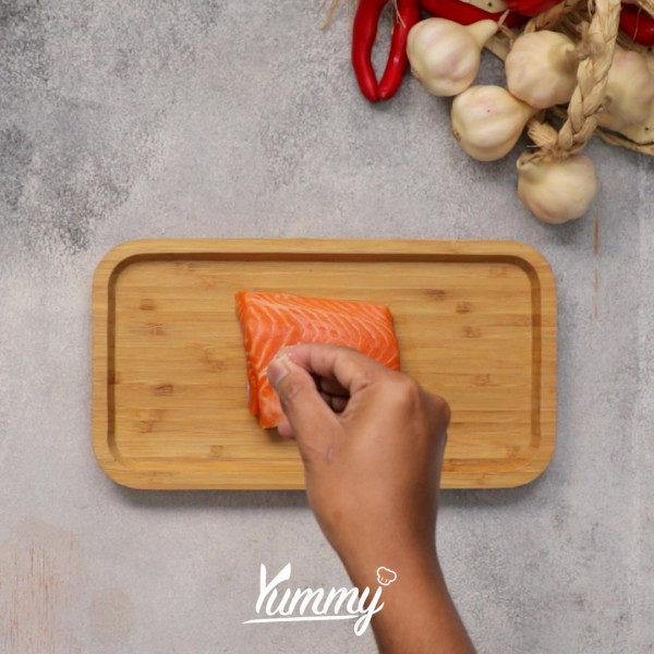 Taburkan lada dan garam di permukaan salmon lalu balur kulit salmon dengan bubuk santan. Panaskan minyak zaitun di atas teflon lalu tambahkan bawang putih.