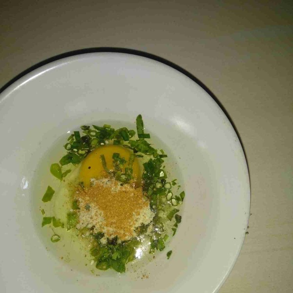 Masukkan telur ke dalam mangkuk, bumbu mie gelas, irisan cabai, seledri, dan daun bawang.