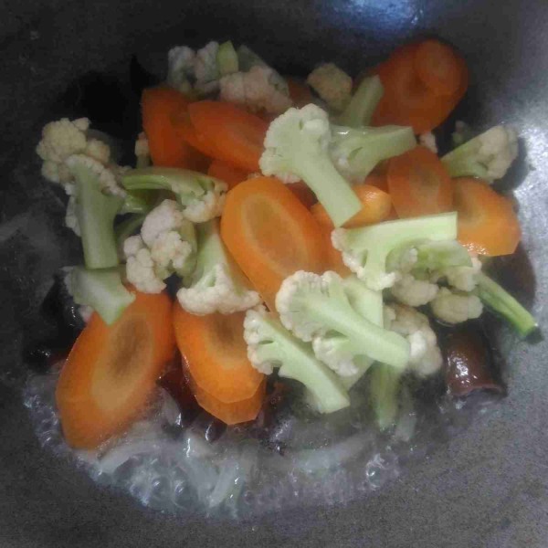 Setelah bawang matang tambahkan air, masukkan wortel, jamur kuping, dan bunga kol, masak hingga wortel dan bunga kol empuk.
