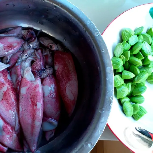 Buang tulang cumi, cuci badan cumi tapi jangan buang tintanya. Kupas petai dan potong jadi dua bagian