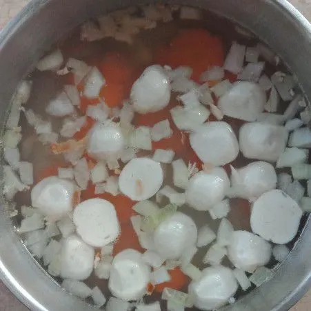 Masukkan air, masak hingga mendidih, lalu masukkan wortel dan bakso ikan. Masak hingga setengah matang