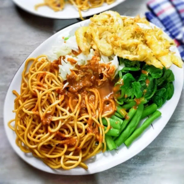 Tata bakmie dan sayuran dalam piring saji. Tuang bumbu pecel