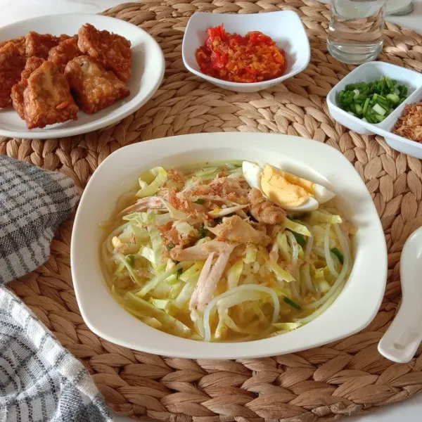 Tata nasi dalam piring saji beri soun, rajangan kubis, suiran ayam lalu guyur dengan kuah soto dan lengkapi dengan potongan telur rebus serta taburan bawang merah goreng