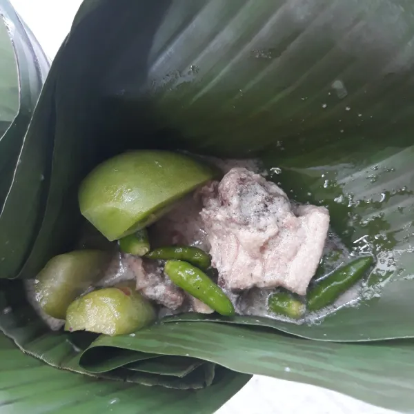 Ambil 2 lembar daun pisang pisang, tata tomat, belimbing wuluh, dan cabai rawit. Tambahkan 2 potong ayam, bentuk seperti tum lalu tusuk dengan tusuk gigi