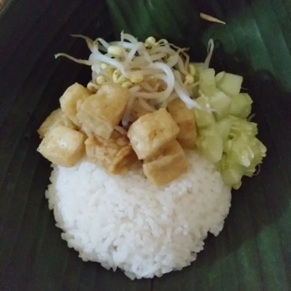 Tata nasi putih, tahu, tempe, tauge rebus dan potongan timun di atas daun pisang