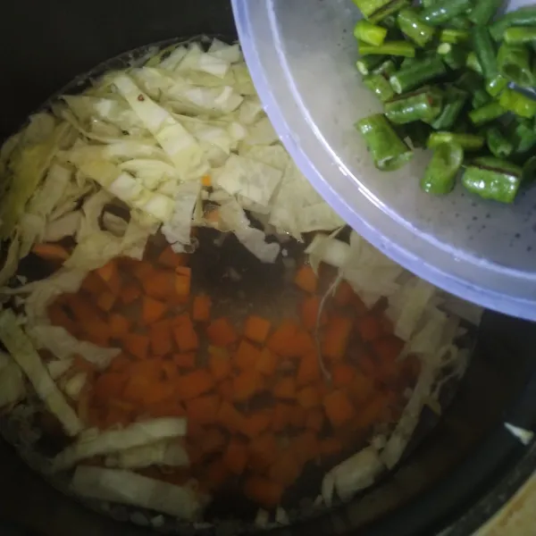 Masukkan irisan wortel, kacang panjang, dan kol. Tambahkan garam, lada, dan kaldu ayam. Aduk dan tutup magicom selama 10 menit.