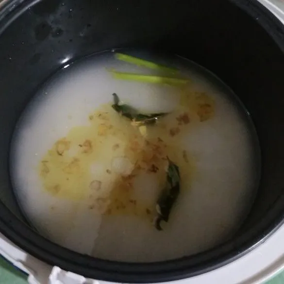 Masukkan tumisan bawang ke dalam panci rice cooker yang sudah berisi beras.