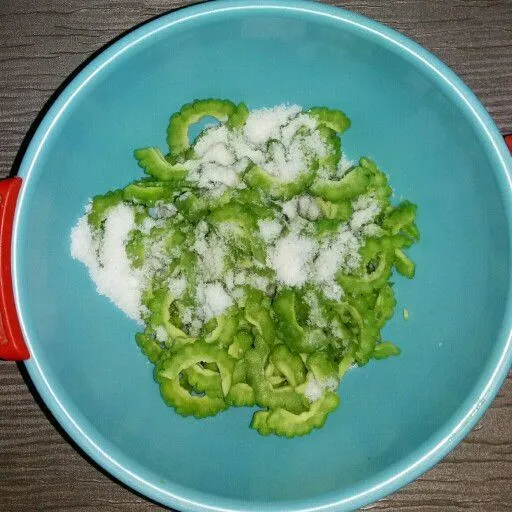 Belah pare, buang bagian tengahnya. Iris agak tipis. Bubuhi 1.5 sdm garam lalu aduk/kocok rata, tidak perlu di remas.