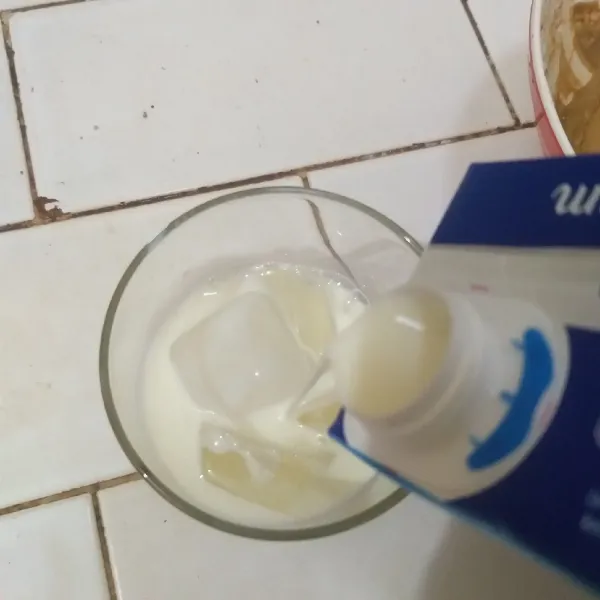 Tata es batu di dalam gelas, tuang susu UHT sampai setengah gelas lebih sedikit.