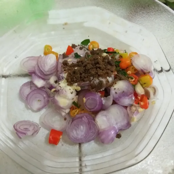 Pindahkan ke mangkuk, beri terasi sangrai. Tuangi minyak kelapa panas, aduk rata