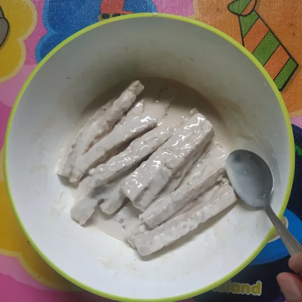 Masukkan potongan tempe ke dalam adonan tepung bumbu, aduk rata agar semua tertutup adonan, biarkan 15 menit agar meresap