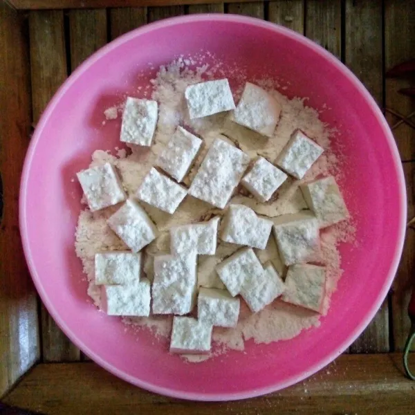 potong dadu tahu putih, cuci bersih. lalu balur dengan tepung bumbu instan, hingga terlapisi semua bagiannya