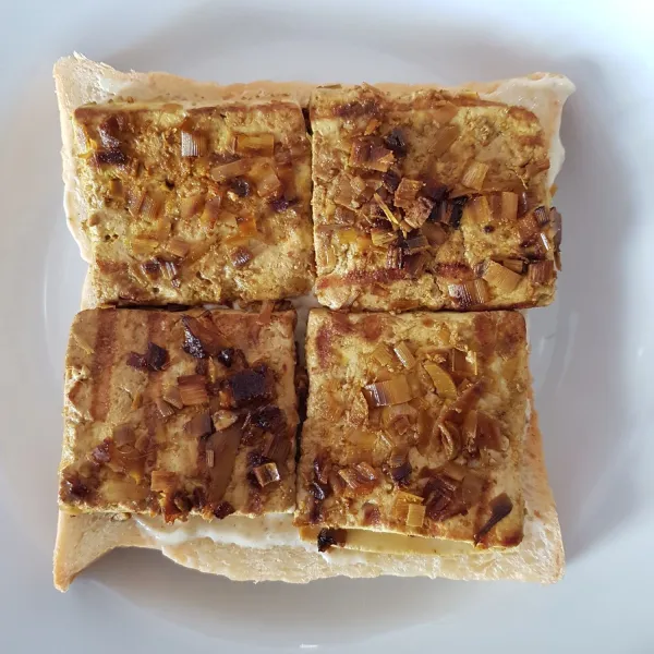 Siapkan 1 lembar roti tawar kemudian beri bahan olesan, tambahkan tahu panggang di atasnya