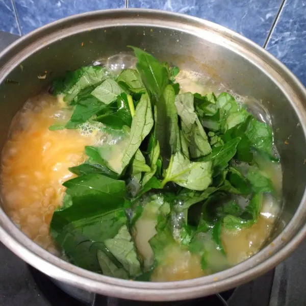 Setelah nasi menjadi bubur, masukkan irisan daun laksa dan daun gedi. Aduk rata
